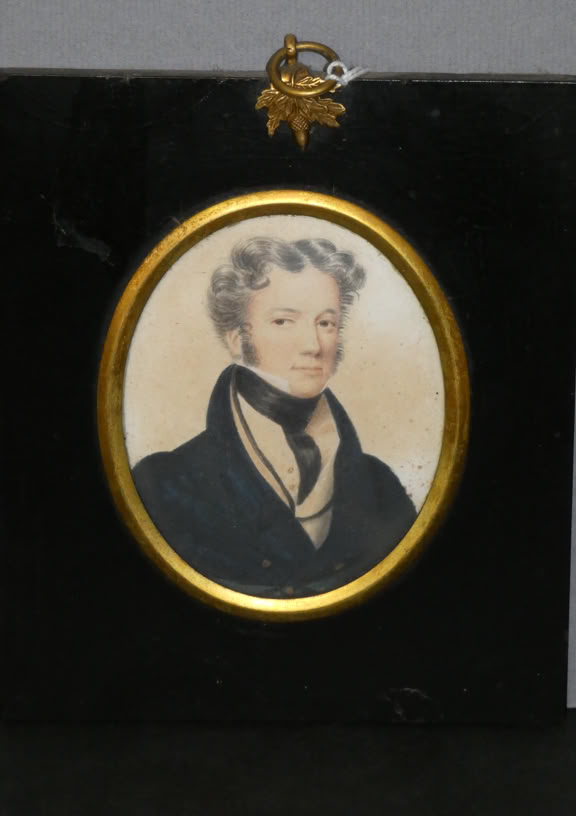 Oval portrait of a person with short, curly hair, wearing a dark coat and a light-colored scarf, set in a gold frame on a black rectangular background.