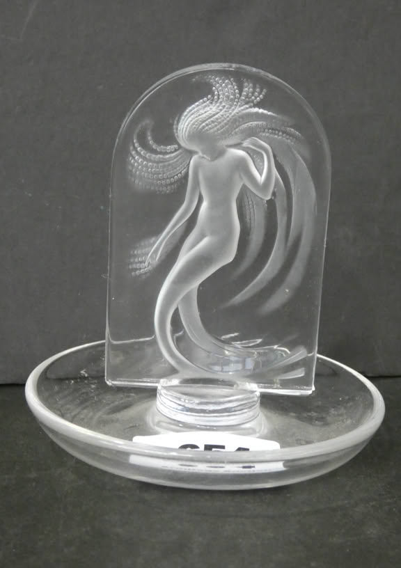 A clear glass sculpture featuring an etched figure with flowing hair, set on a round glass base.